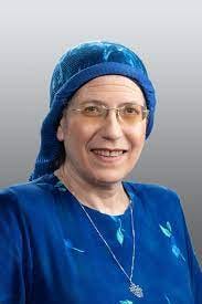 Portrait of MK Orit Malka Struck, a woman in her 60s wearing blue dress, blue headscarf, and glasses