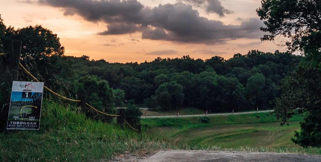 View from a disc golf teeing area high up on a hill overlooking a steep drop at sunrise