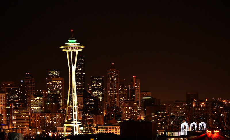 A nighttime photograph of the Seattle skyline. The Space Needle is illuminated brightly in the foreground.