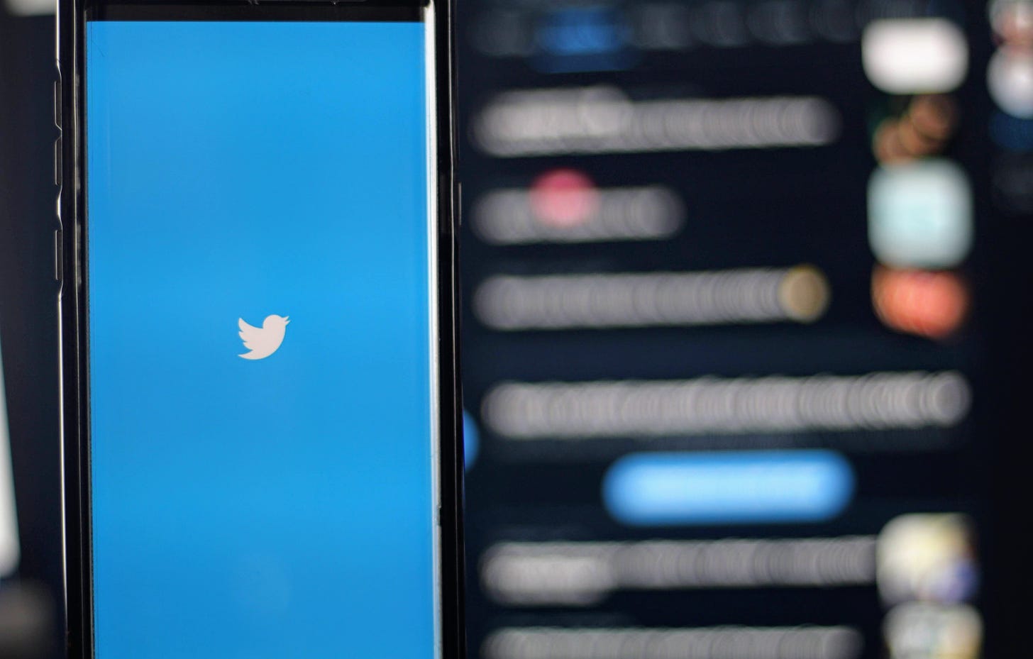 Photo illustration of the Twitter app against a blurred backdrop of tweets (Joshua Hoehne / Unsplash)