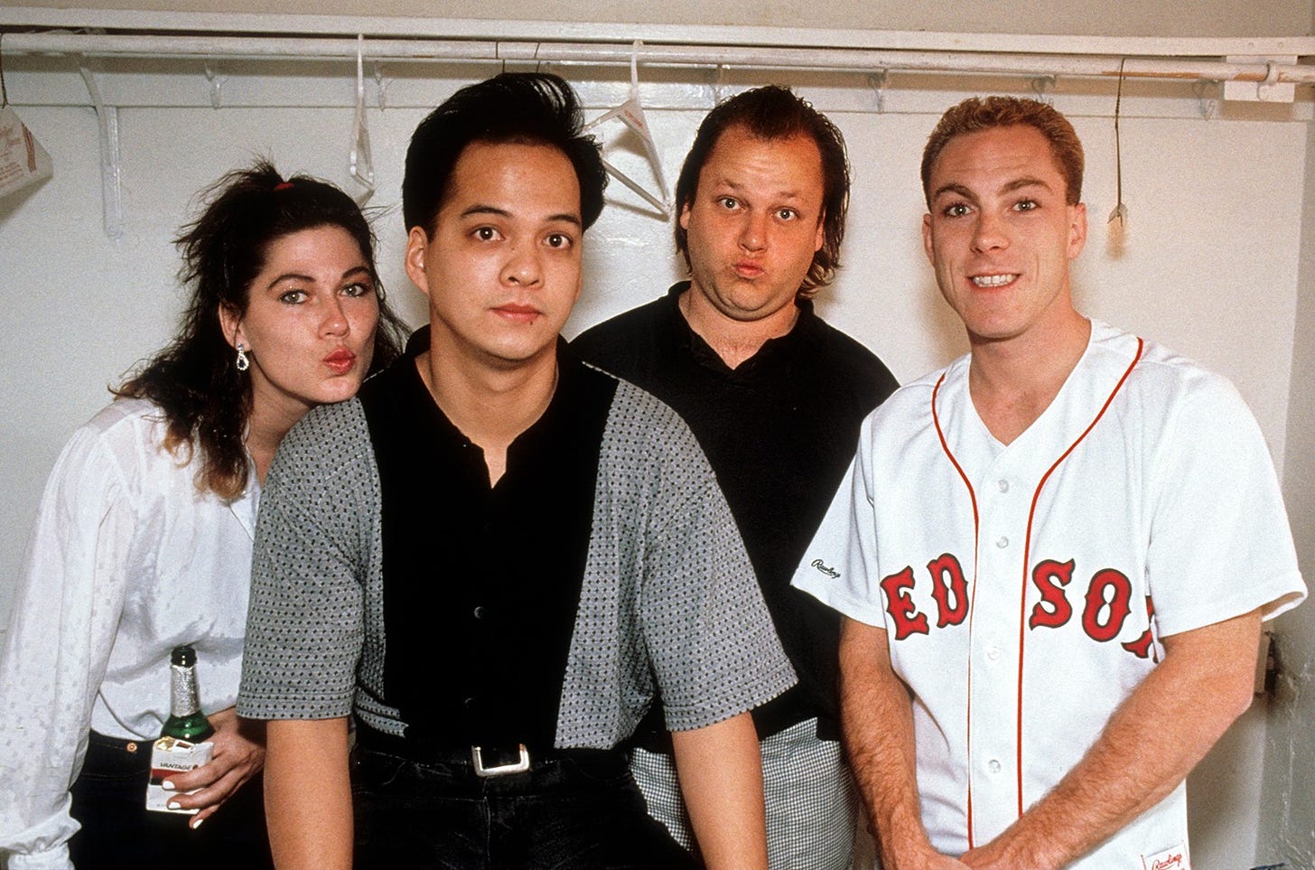 Left-Right: Kim Deal, Joey Santiago, Black Francis, and David Lovering. They're in what appears to be a changing room with a white wall; David and Joey are looking serious but Kim and Francis, standing slightly further back, are making strange faces.