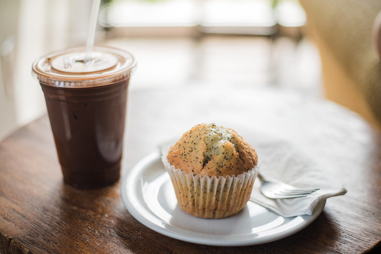 a poppyseed muffin on a plate and a cup of ice coffee