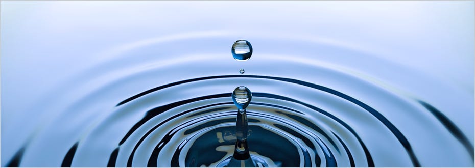 Drops of water fall on a liquid surface creating a large ripple.