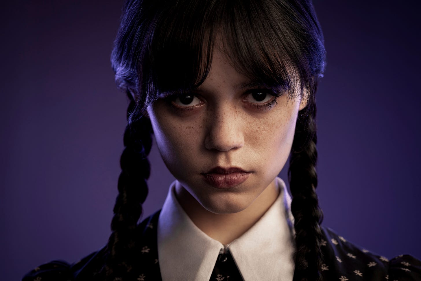 Picture of Jenna Ortega as Wednesday, with purple background and her in the trademark black braids and puritan style dress, looking deadpan at the camera
