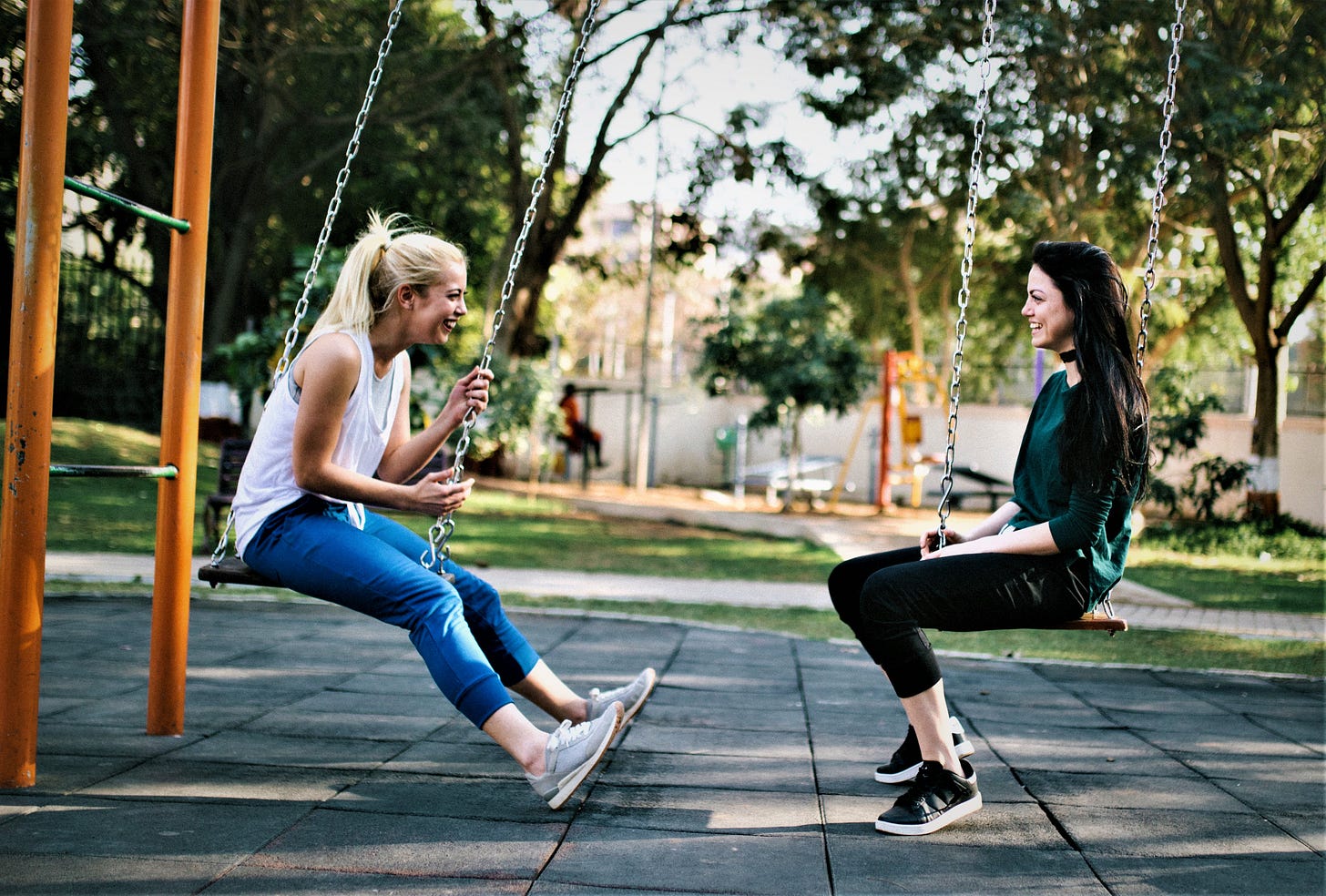 Two happy girls sitting on swings and facing each other