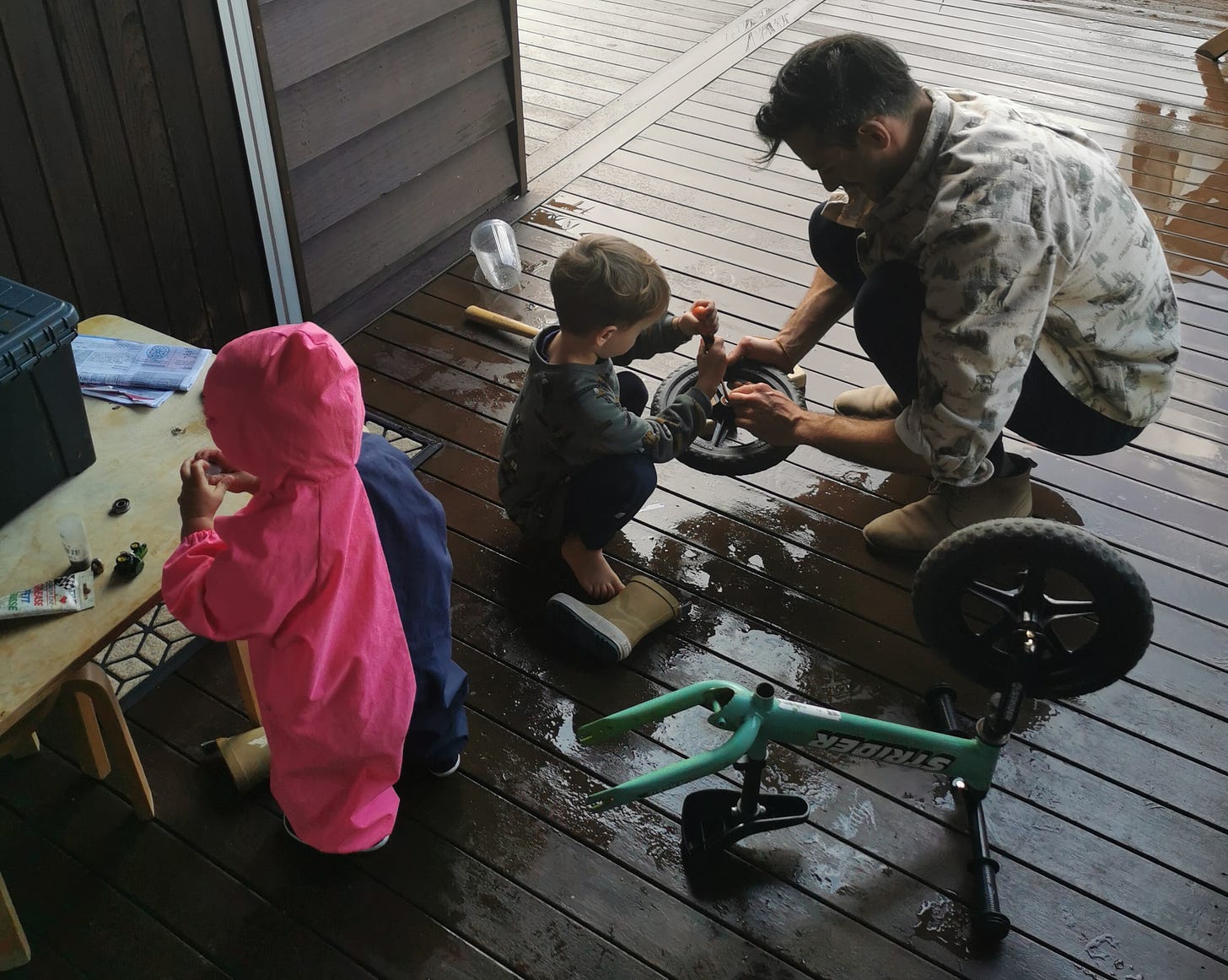 Father and his two sons fixing a kid's bike wheel on a deck in the back garden.