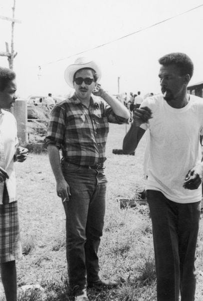 An image tentatively identified as taken at a barbeque hosted by Mr. Steptoc for SNCC staff in McComb, Mississippi. The man in the center wearing a hat is identified as Marshall Ganz, a staff member of SNCC (Student Nonviolent Coordinating Committee).