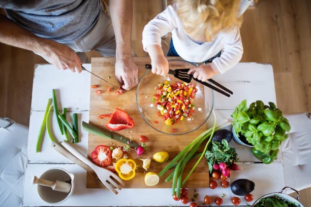 Young father with a toddler boy cooking. Unrecognizable father with a toddler boy cooking. A man with his son making vegetable salad. Top view. family cooking stock pictures, royalty-free photos & images