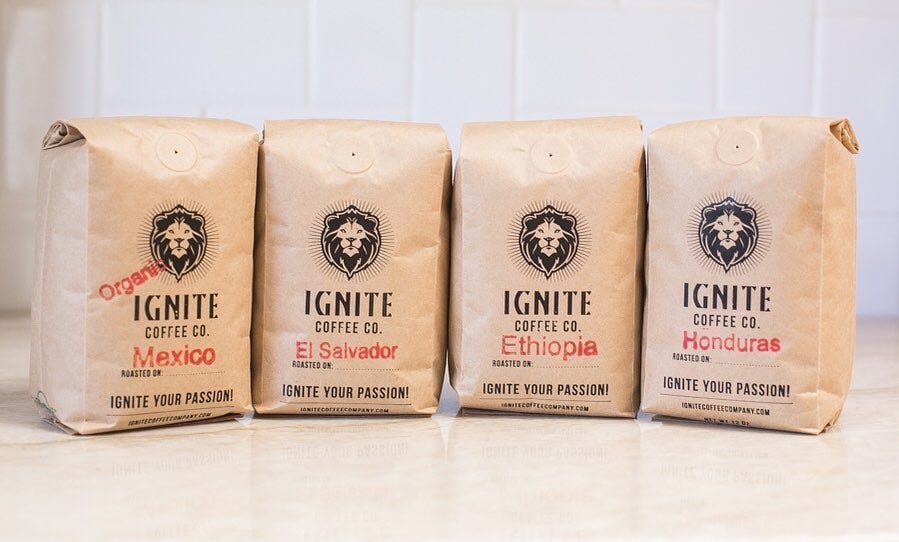 Four bags of coffee with the lion head logo and brand name of Ignite Coffee Co. are lined up facing the camera the countertop is a light white marble with a white wall in the background.