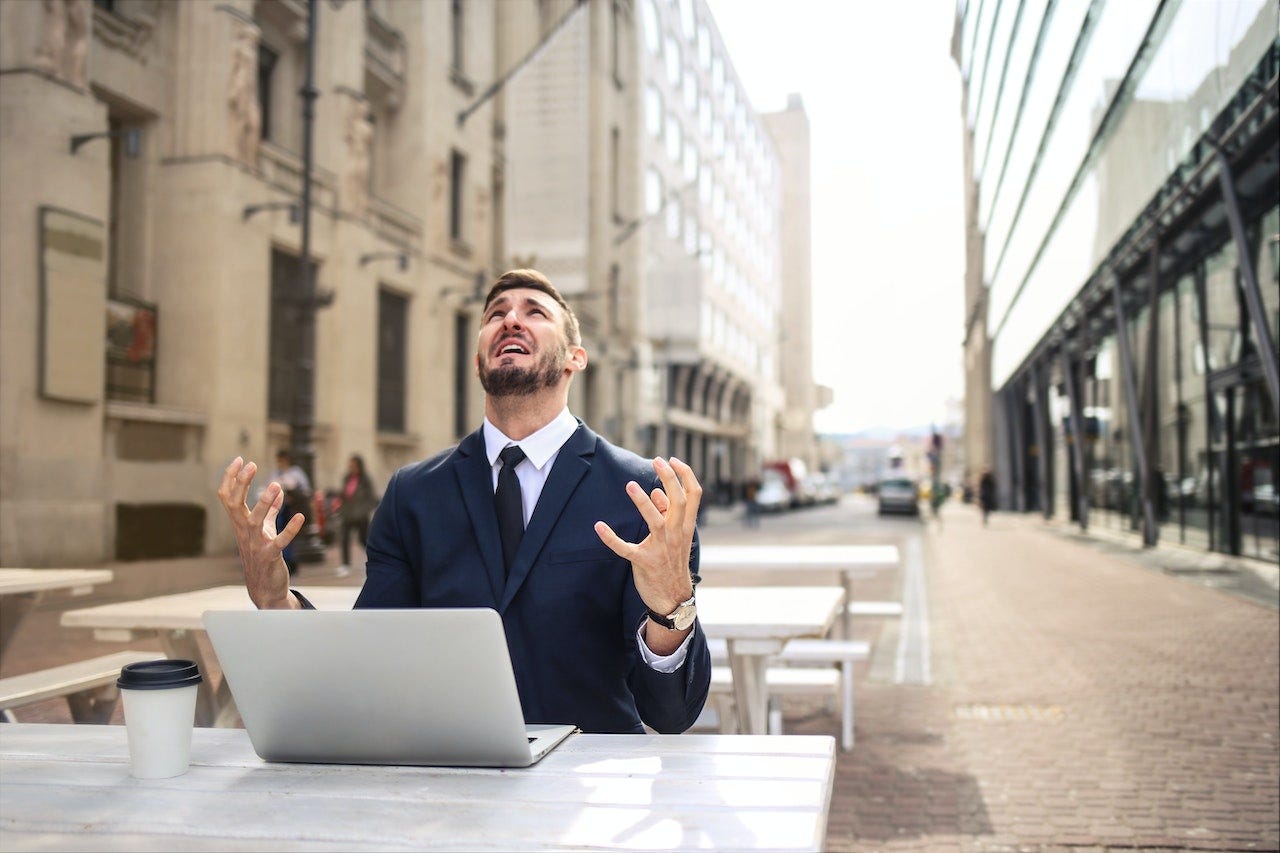 Man looking up at the sky in frustration with a laptop and coffee in front of him