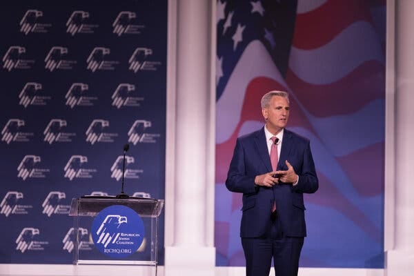 Representative Kevin McCarthy speaking on stage next to a podium that reads Republican Jewish Coalition while wearing a suit.