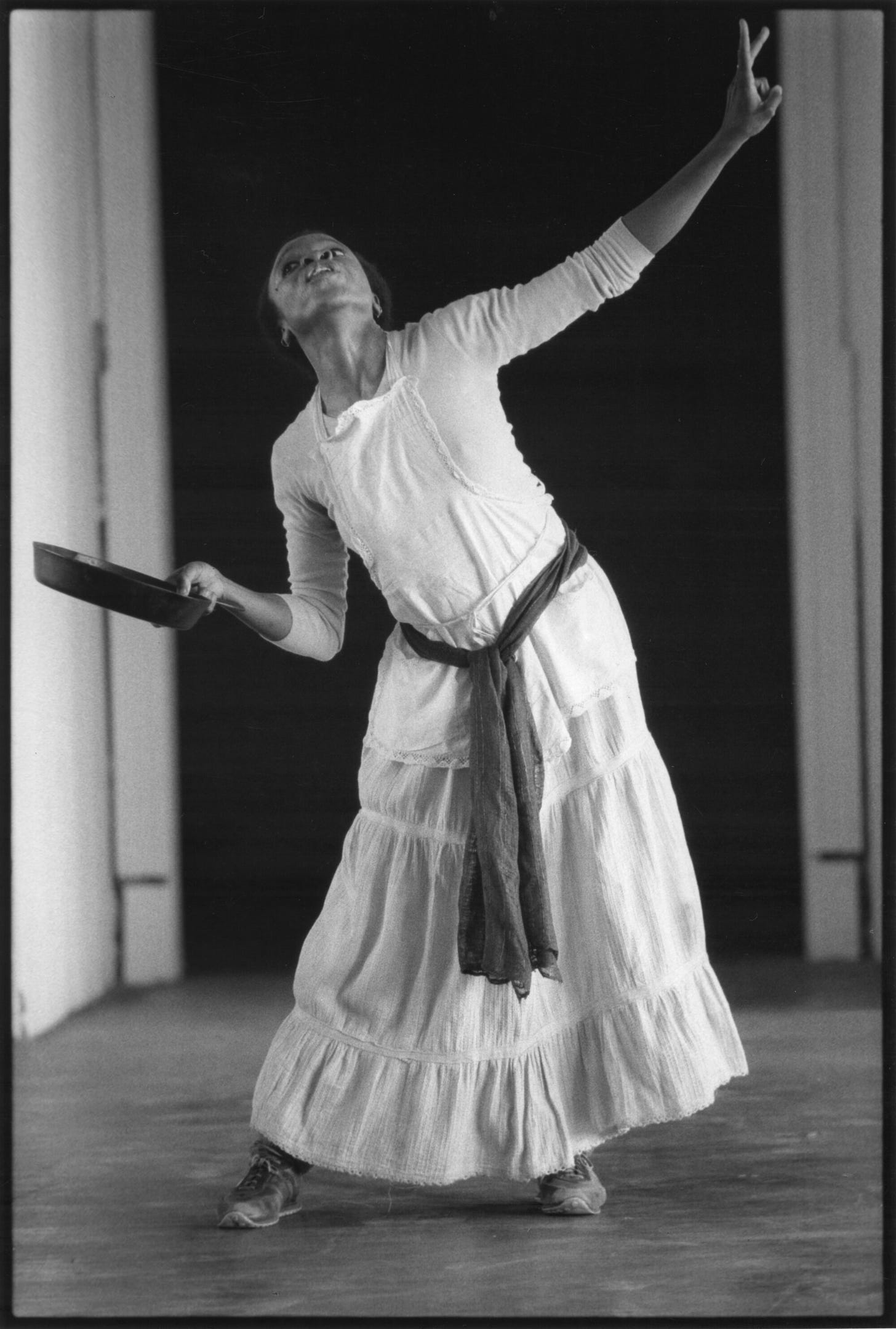 Blondell Cummings dances on stage wearing a white dress and holding a cast iron frying pan