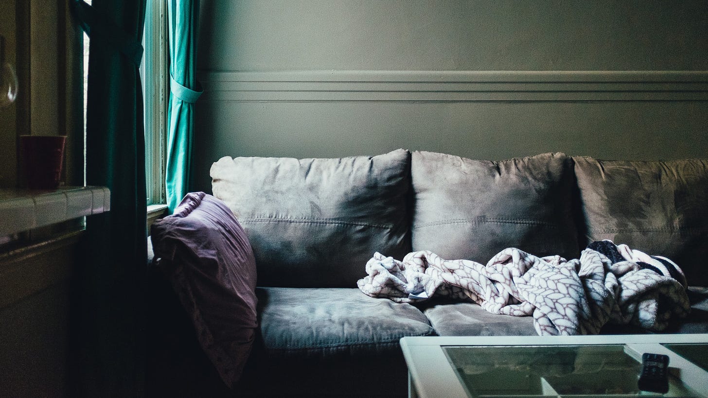Light coming onto gray couch with blanket crumpled on top