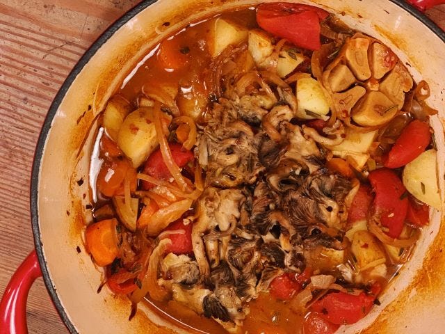 A red Dutch Oven with roasted mushrooms and a vegetables in a red broth.