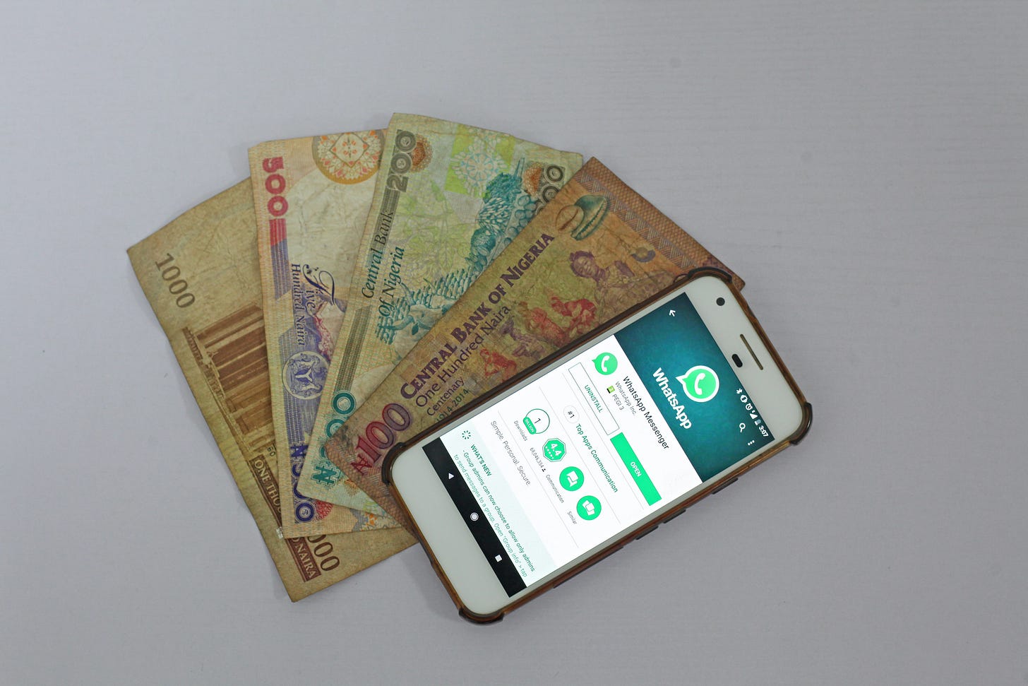 Photo of a phone with WhatsApp open laid on top of currency fanned out underneath it. Benjamin Dada / Unsplash