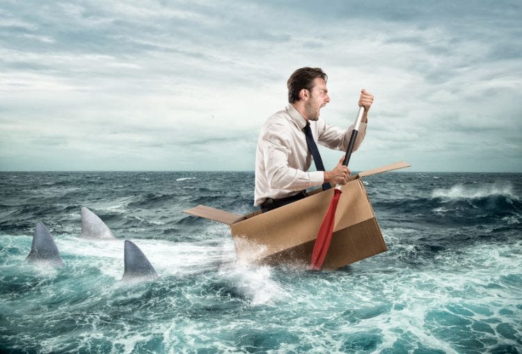 Escape from crisis--a man in a sinking cardboard box rowing from sharks in ocean