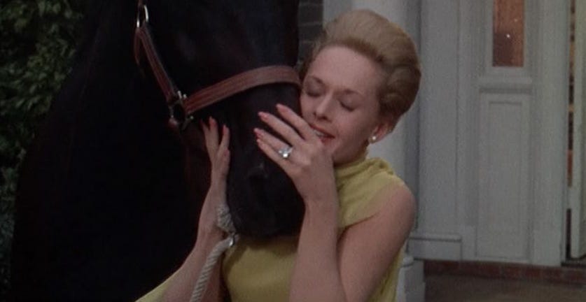 Film still from Marnie. Marnie nuzzles a horse, her wedding ring shining brightly.