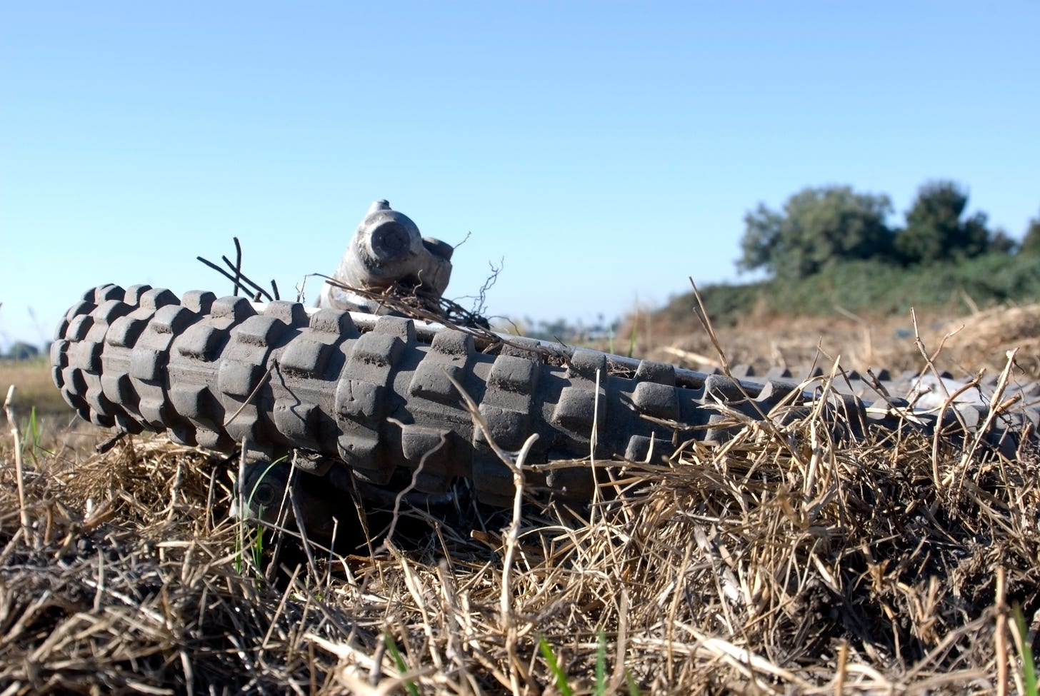 Wheel and muffler of a motocross motorcycle sitting in dry grass on a sunny day