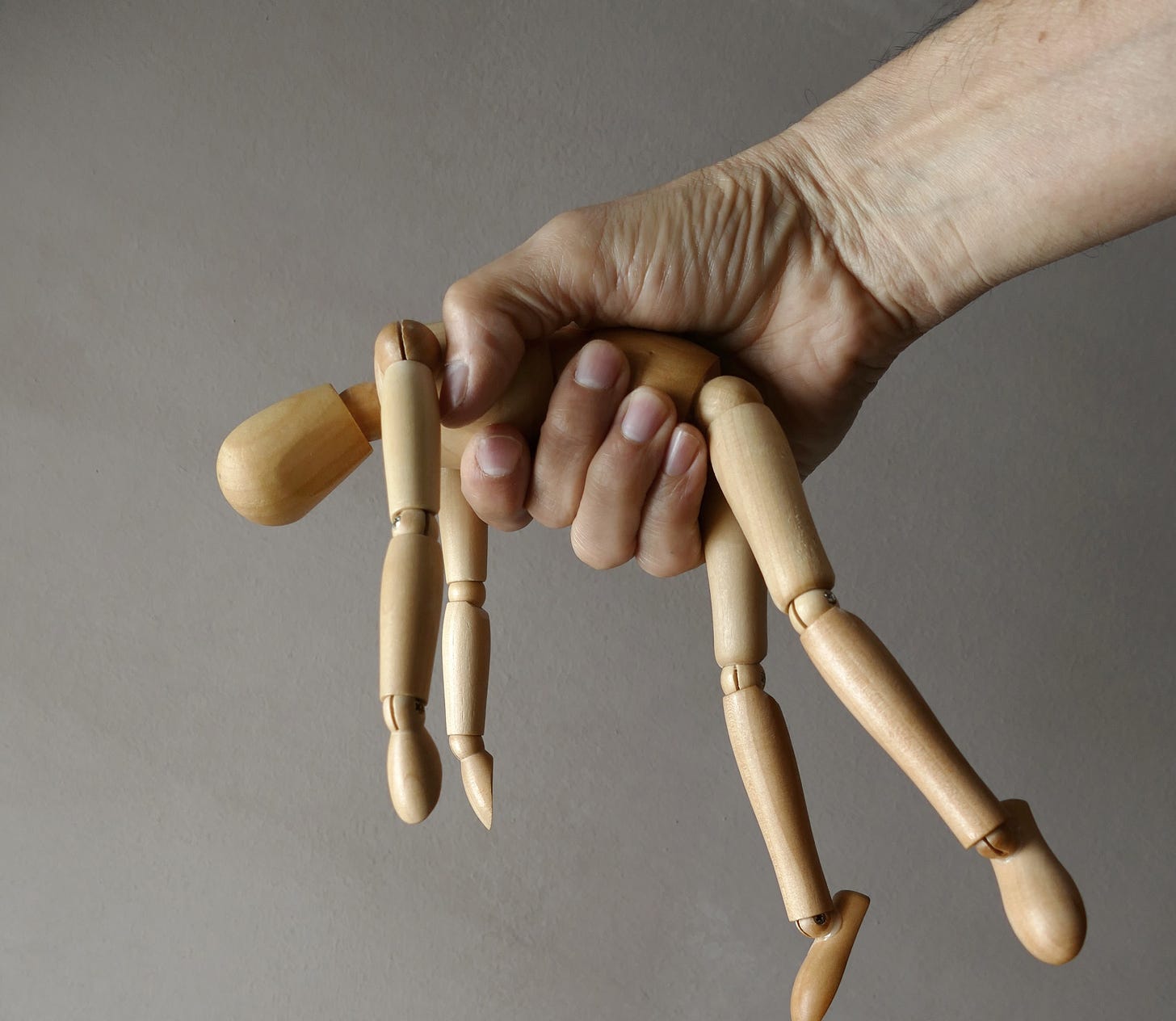 Man's hand crushing wooden doll