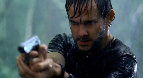 Close up shot of Charlie Pace (Dominic Monaghan) in the rain, pointing a gun. He's brooding very murderishly.