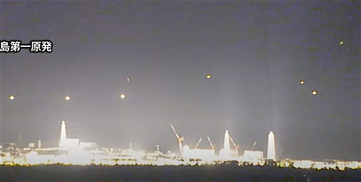 In the night sky, several UFO balls of light hover over the brightly lit Fukushima Daiichi nuclear power station, immediately after the large earthquake in 2011