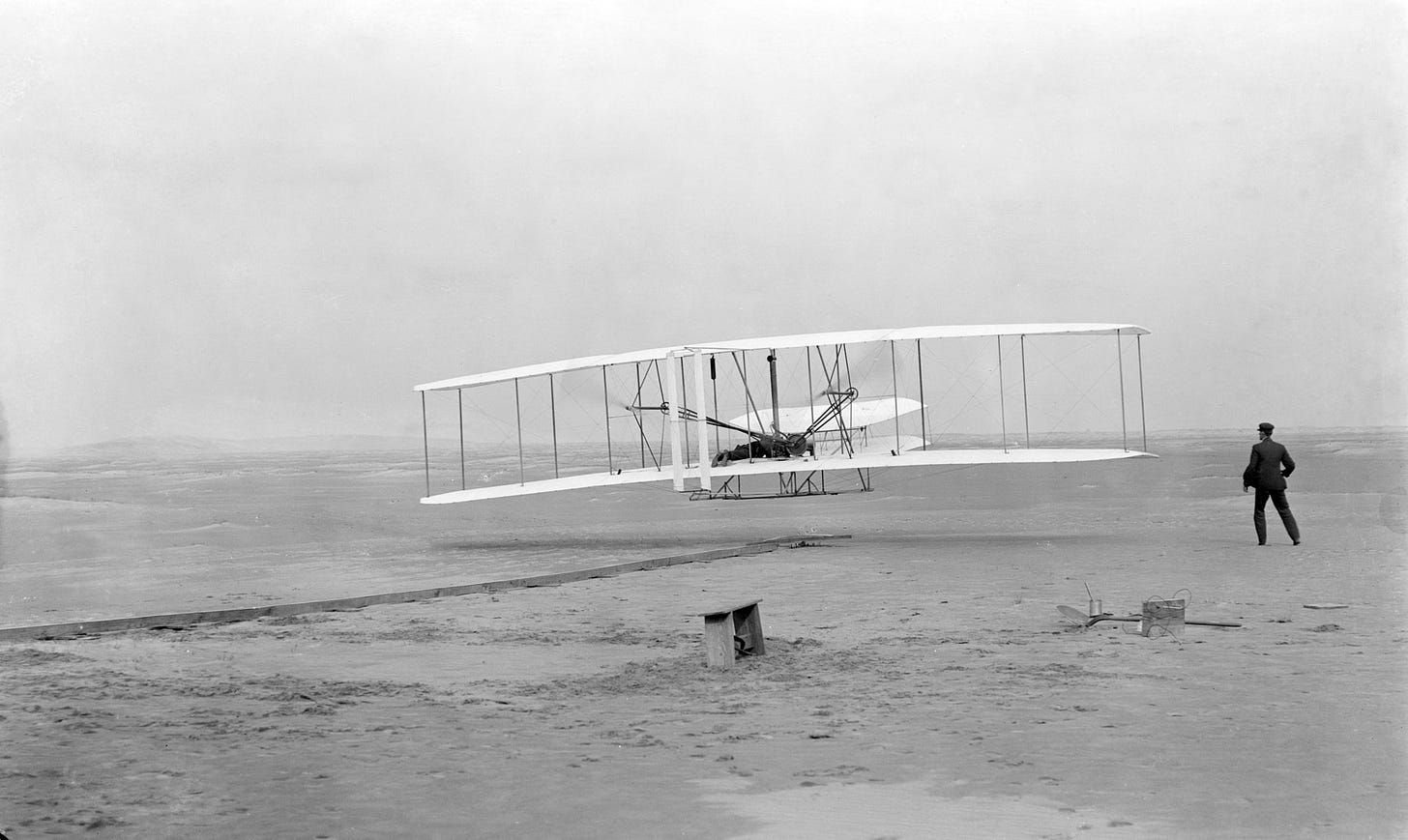 The Wright Flyer's first flight. Orville is piloting while Wilbur runs near the tip of the wing.