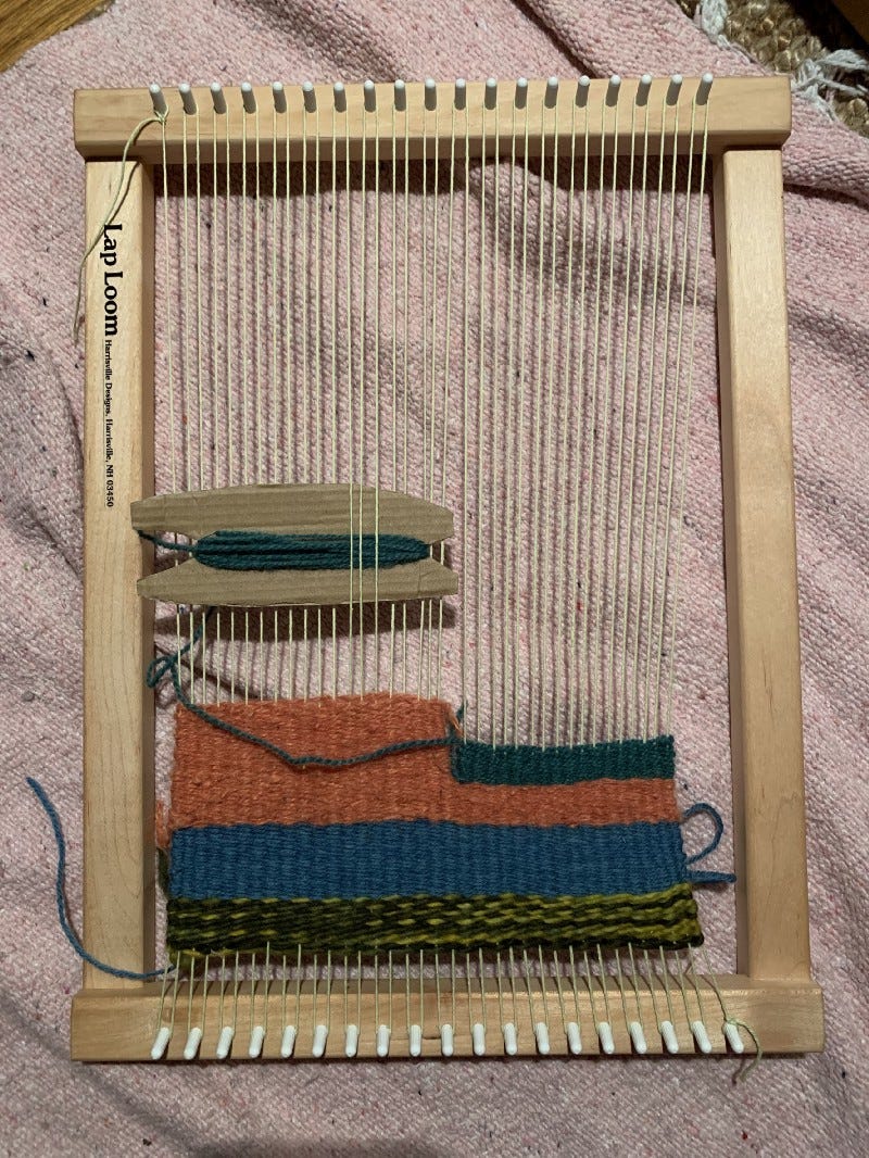 A small loom, partially woven with different colors of yarn.
