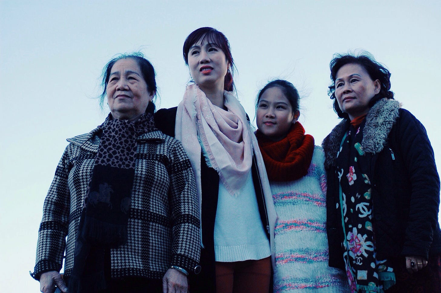 Four generations of Asian women stand in a group and look forward together.