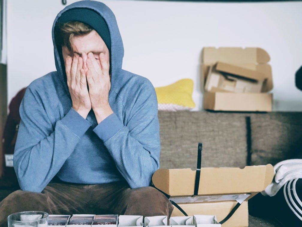 person in blue hoodie sits on couch with head in hands