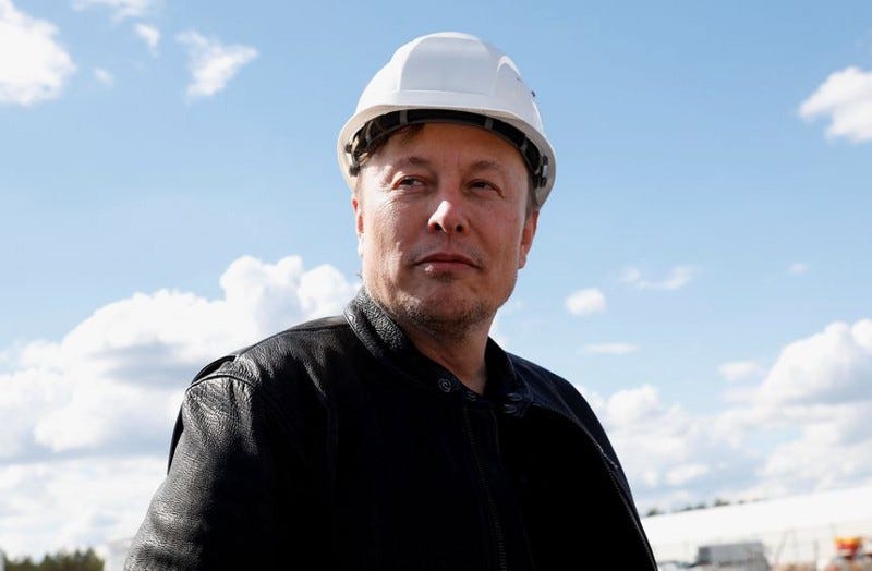 Elon Musk looking smug in a white hard hat.