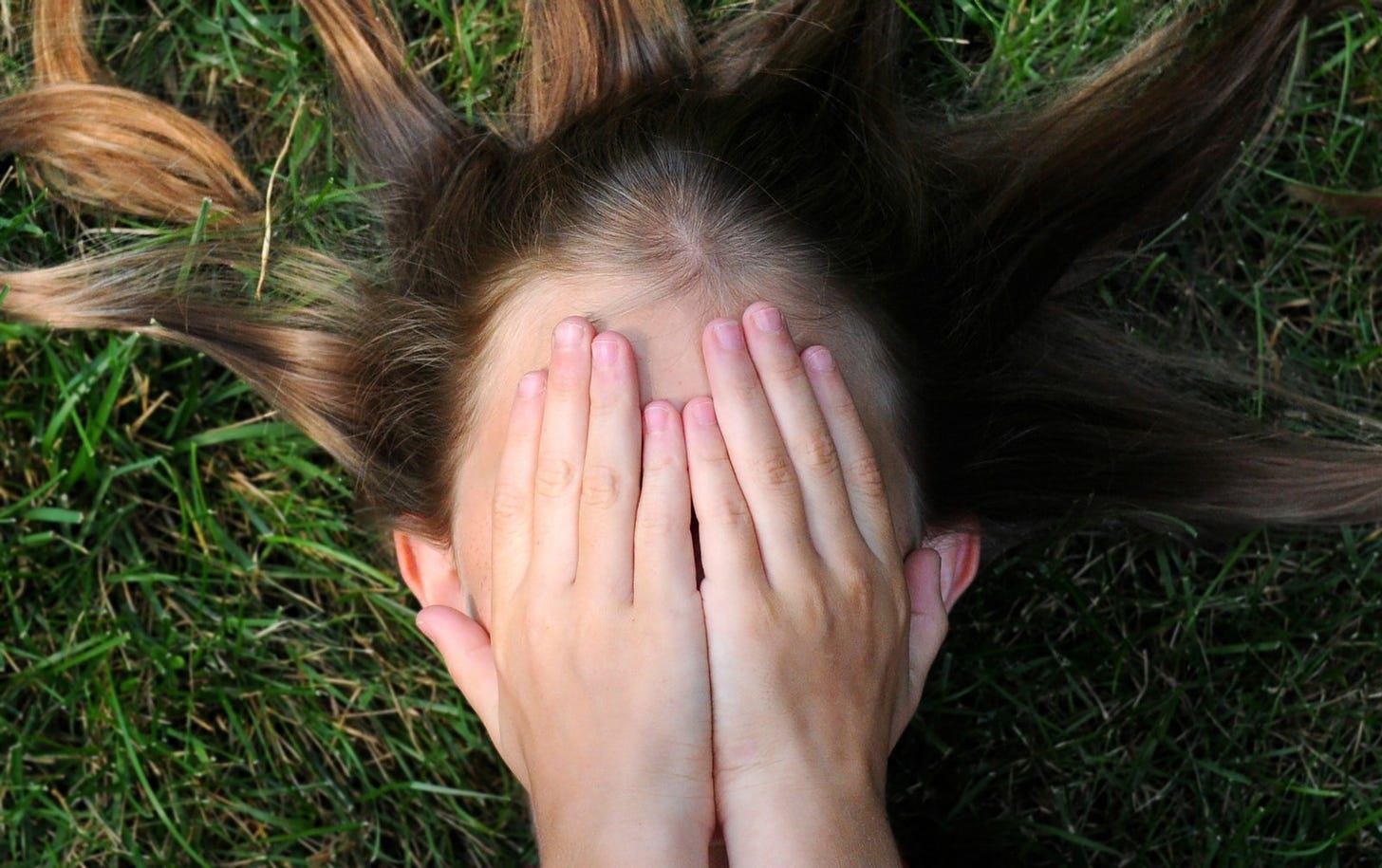 Closeup of a young girl as she covers her face with both hands in fear.