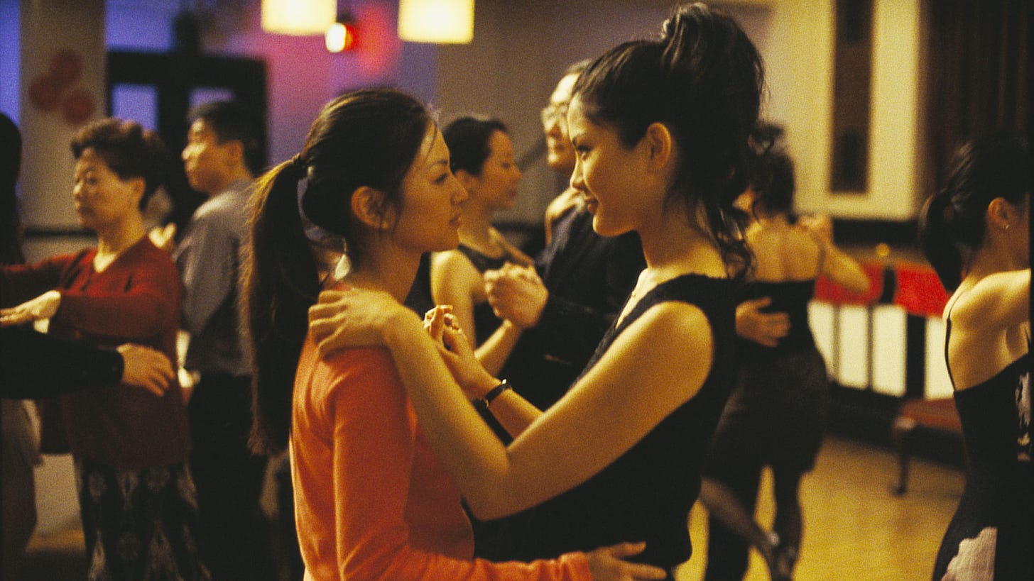 Movie still from Saving Face. Two women hold each others hands while dancing each other, surrounded by other couples in a community hall.