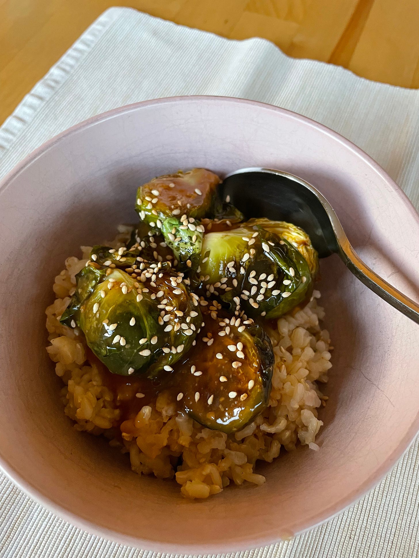 A bowl filled with brown rice, roasted brussel sprouts covered in teriyaki sauce and sprinkled with sesame seeds.