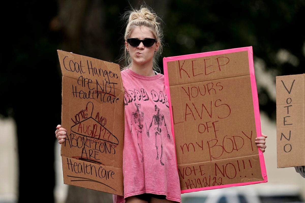 An abortion rights protester holds signs, one of which reads, “Keep your laws off my body.”