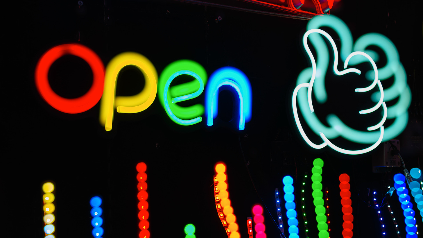 Picture of neon sign saying open with a neon thumbs up at night.