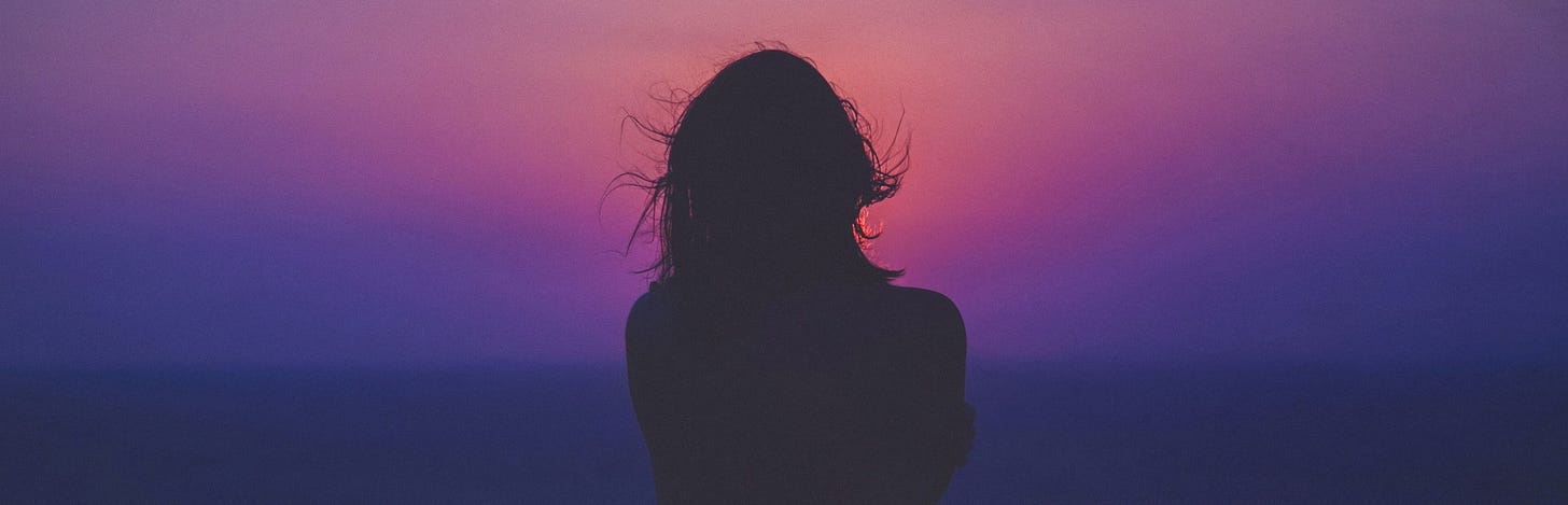 The silhouette of a woman looking pensively at a blue and deep purple sunset. This image is a spacer.
