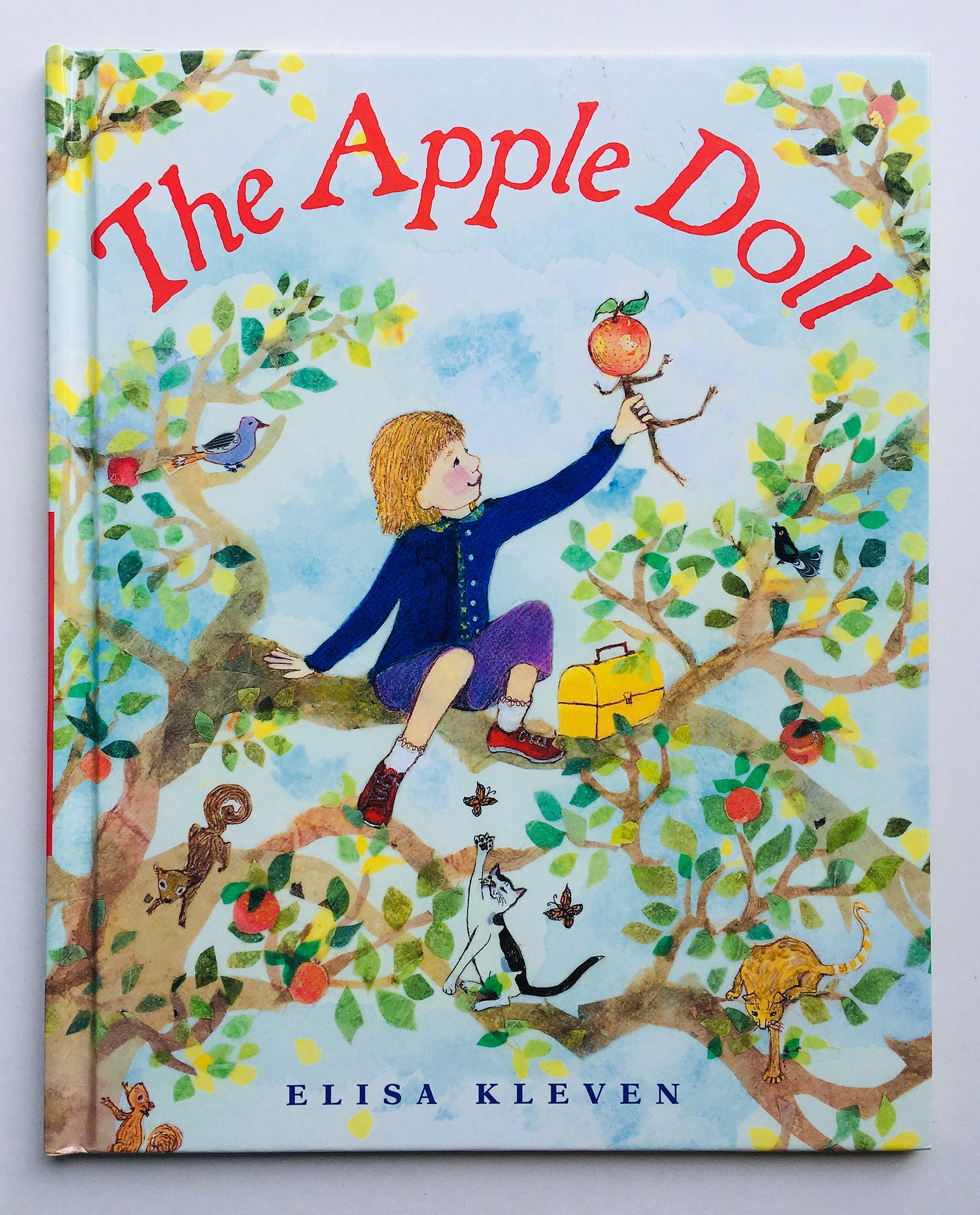 A girl sits on a branch of an apple tree, playing with an apple doll