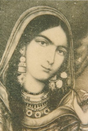 A sepia toned picture of a lady tilting her head towards the right. She has jewels on in her ears and neck, and a dupatta covering most of her hair. 