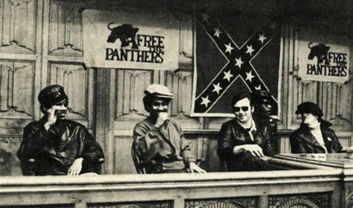 Two Black Panthers with two Young Patriots at the table, Free the Panther Flags and Confederate Flag.
