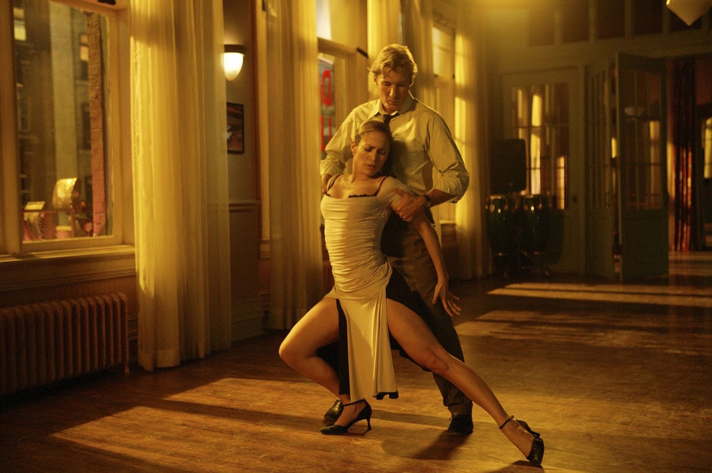 A white man, played by Richard Gere, dances seductively with a Latina woman, played by Jennifer Lopez, in an empty ballroom