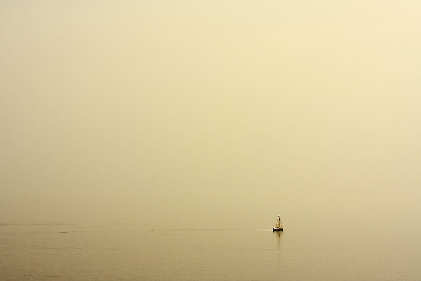 A photograph of a small, solitary sailboat on a lake. It's hazy and foggy. The picture conveys a sense of loneliness and isolation.