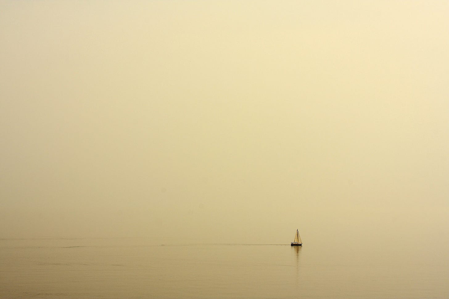 A photograph of a small, solitary sailboat on a lake. It's hazy and foggy. The picture conveys a sense of loneliness and isolation.