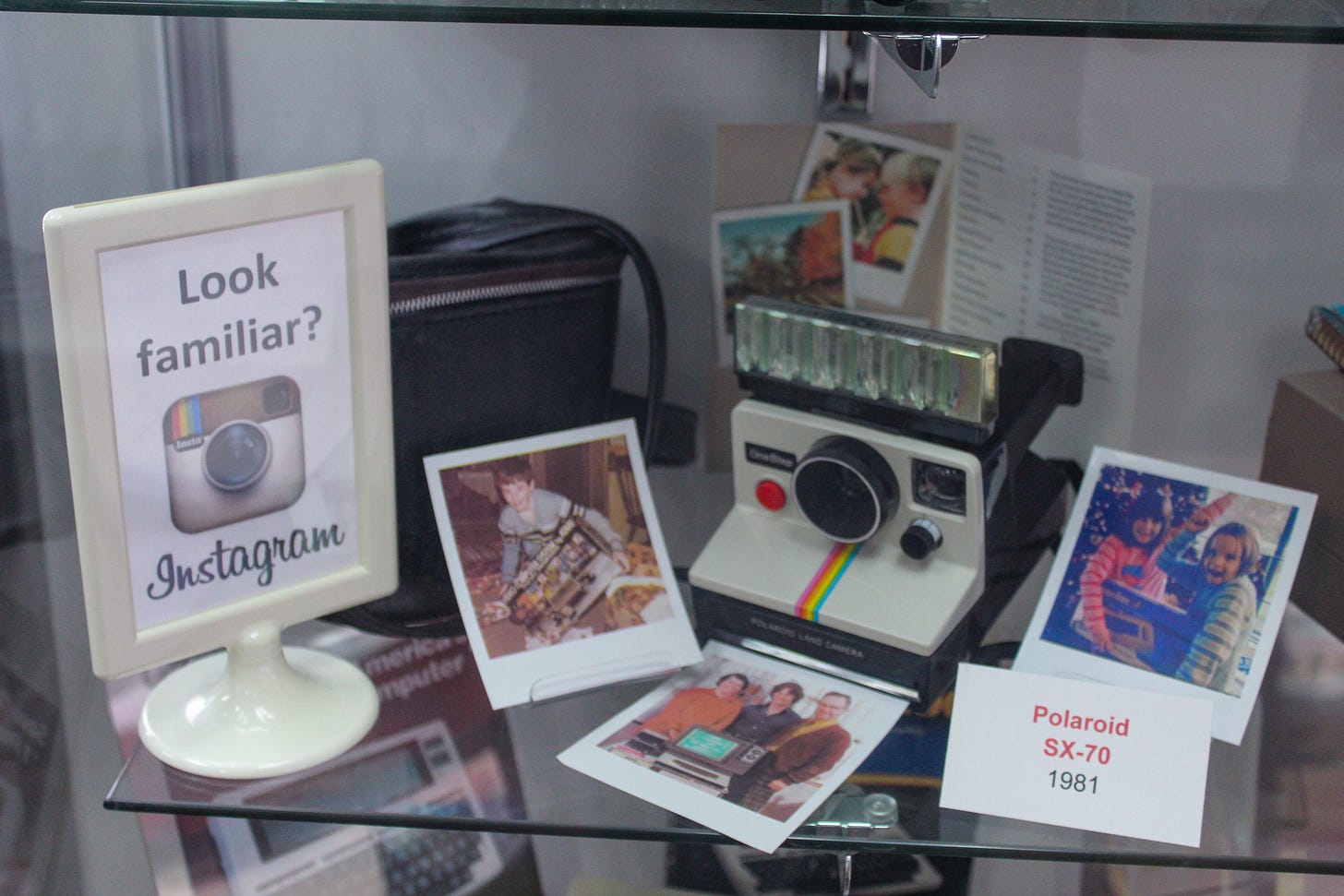 A Polaroid camera and Polaroid prints inside a glass display case