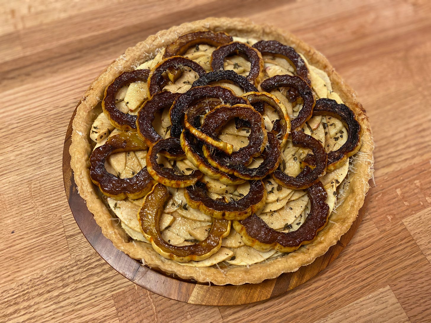 A round tart layered with apple slices and dark, golden brown rings of roasted delicata squash.