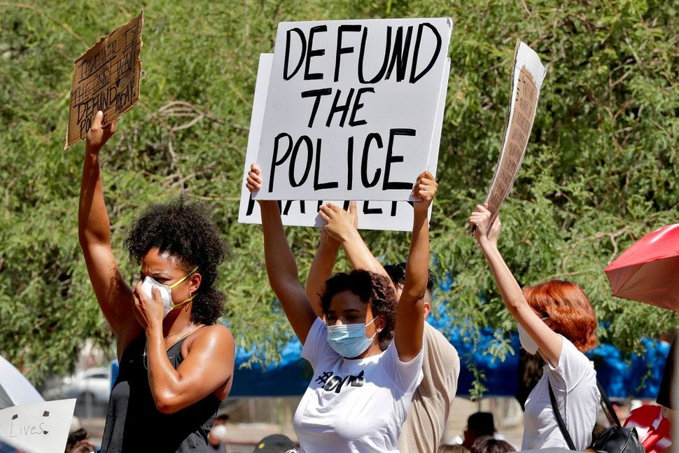 Protesters holding signs that say "defund the police" at a protest