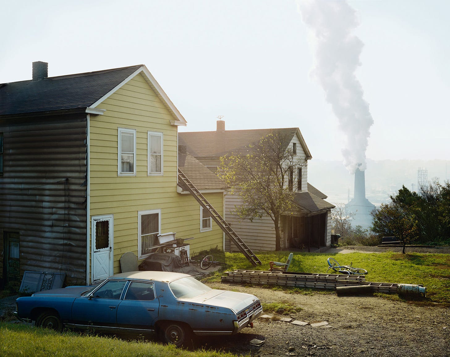 Two run-down houses on a hill with smokestack of steel mill just beyond