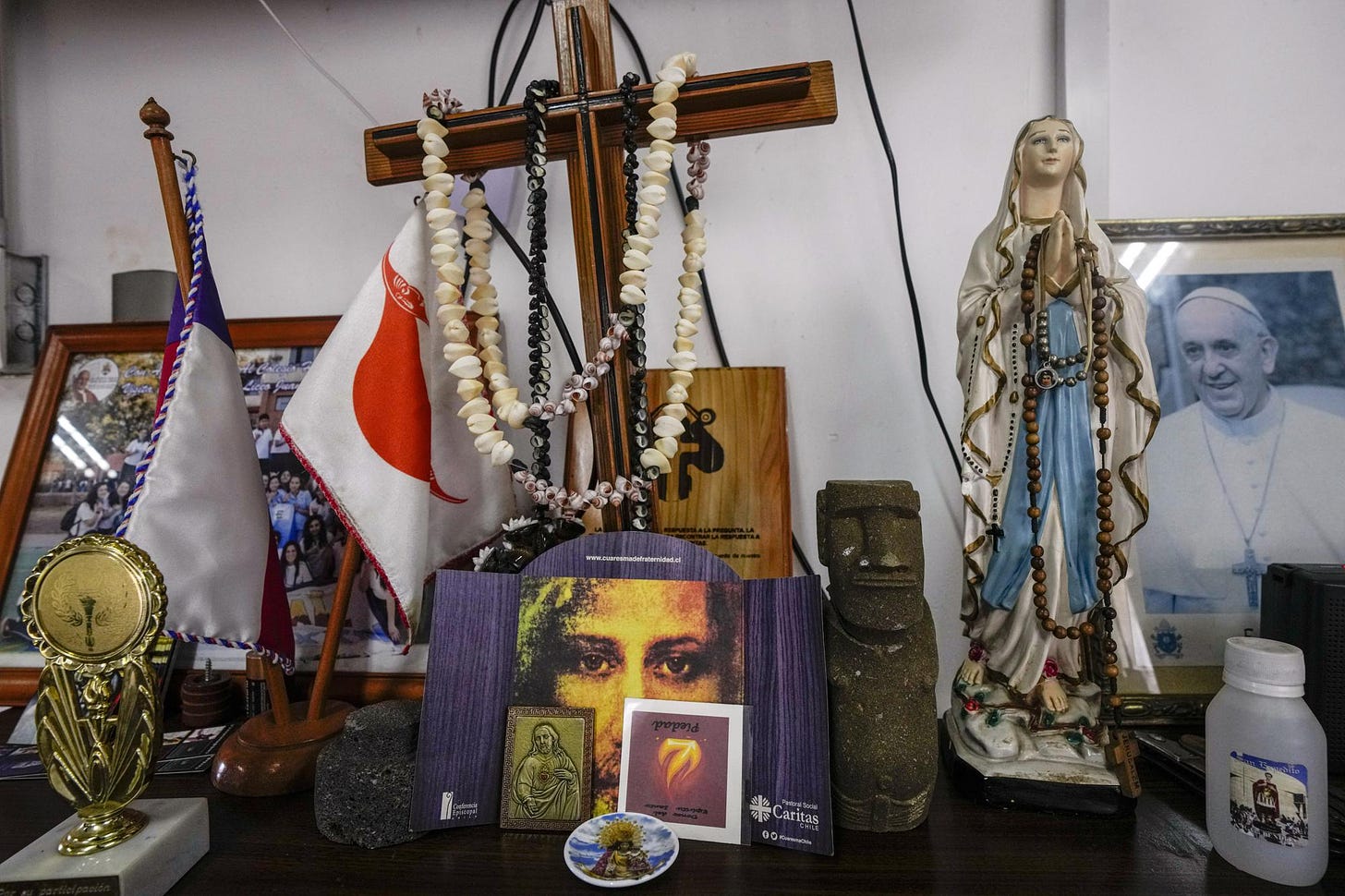 A small replica of a moai statue stands on an altar with religious iconology in the administration office at the Eugenio Eyraud Catholic school in Hanga Roa, Rapa Nui or Easter Island, Chile, Wednesday, Nov. 23, 2022. The first Europeans arrived to Rapa Nui in 1722, soon followed by missionaries, when Rapanui religiosity began to intertwine with Christianity. (AP Photo/Esteban Felix)