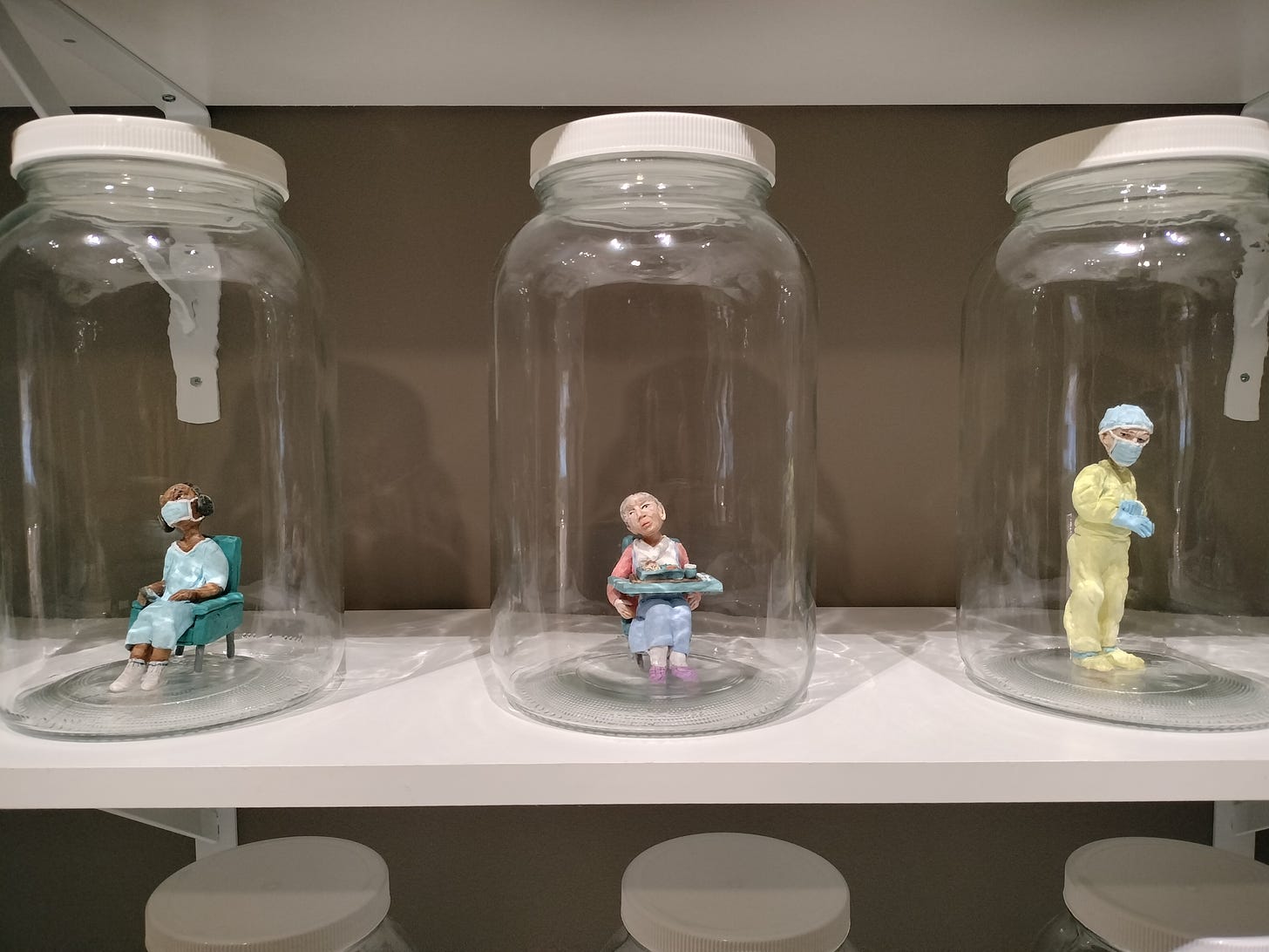 three large jars on a white shelf with sculpted color figures of individual elderly people