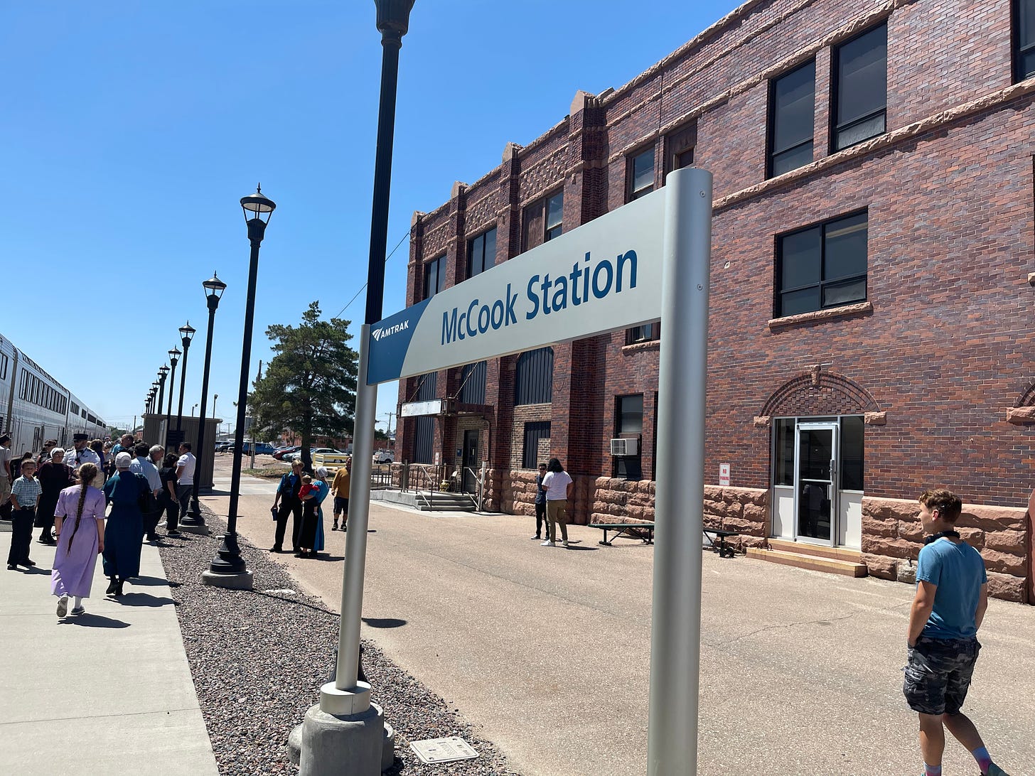 an Amtrak sign for McCook Station in Nebraska, on a concrete platform with a brick building behind