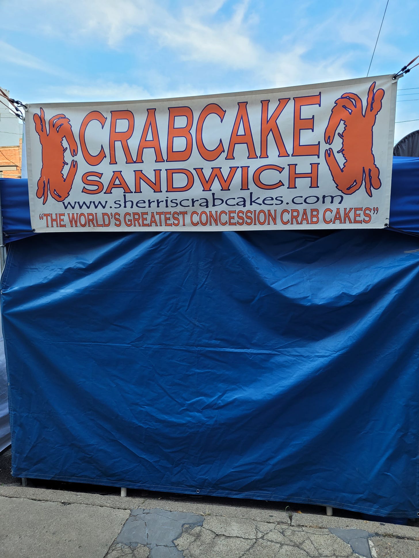 A sign that says "Crab Cake Sandwich World's Greatest Concession Crab Cakes" above a closed street fair tent